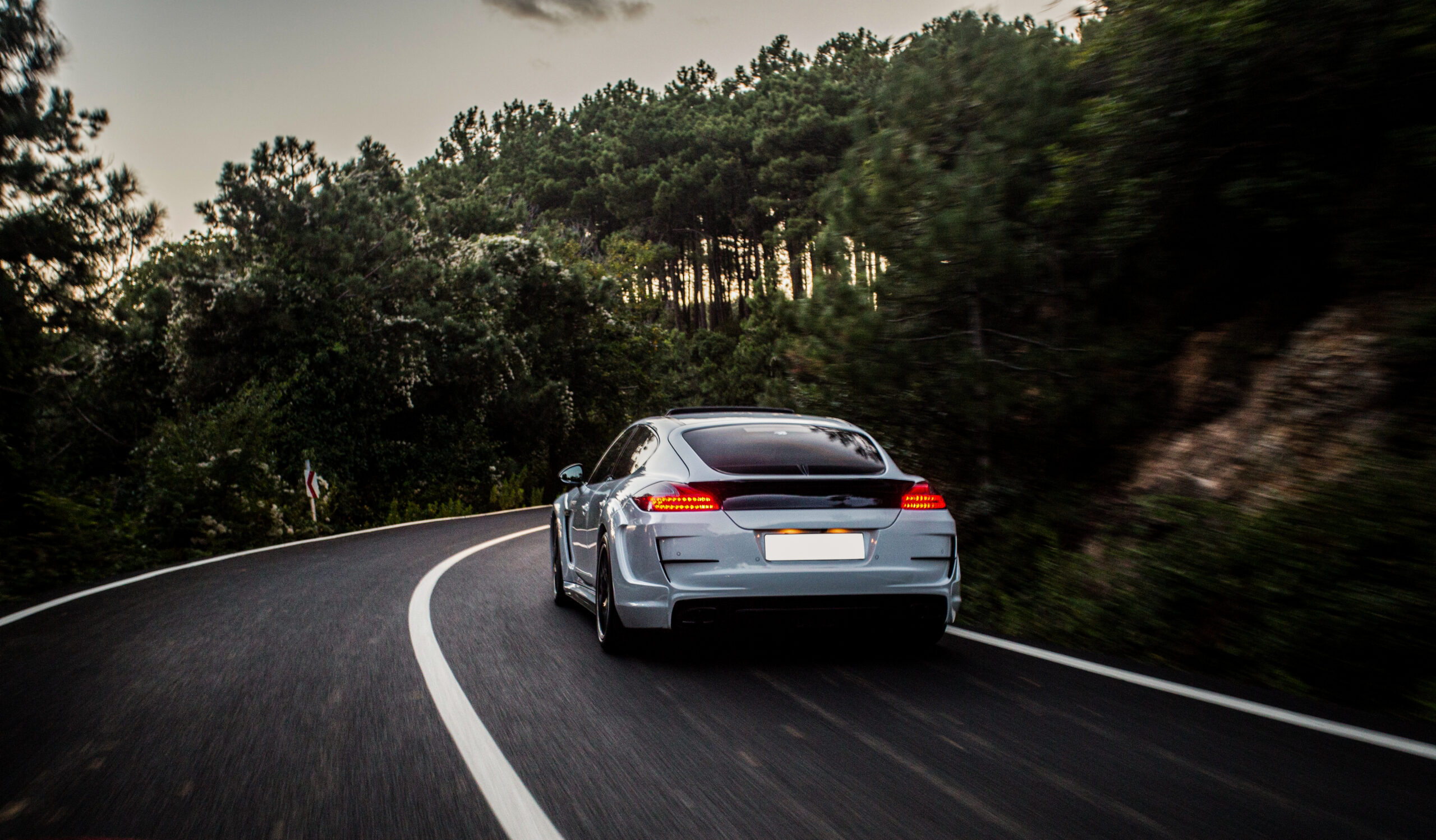 A silver Porsche on a winding road through the forest